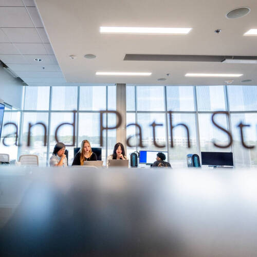 three people working closely on computers in the background, Grand Path Studio door sign appears as if it's written above them on windows